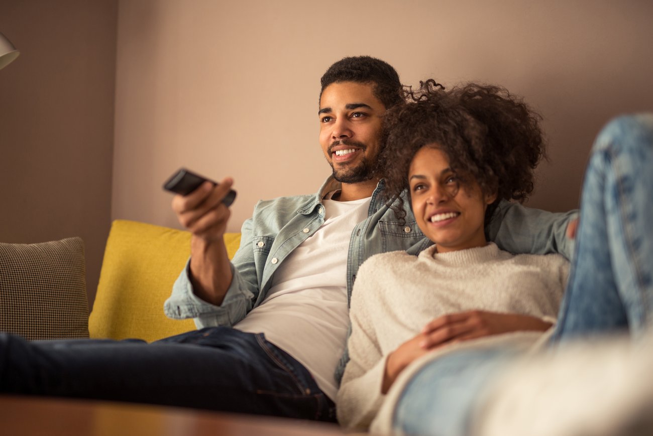 A couple laying on their couch watching TV together