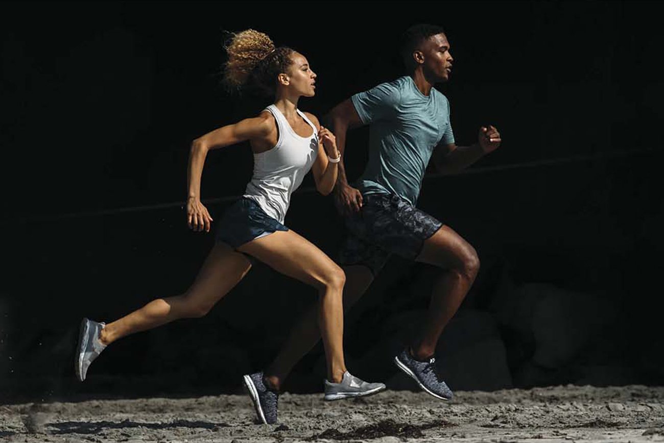 Two runners in Vuori athletic apparel sprinting along a beach.