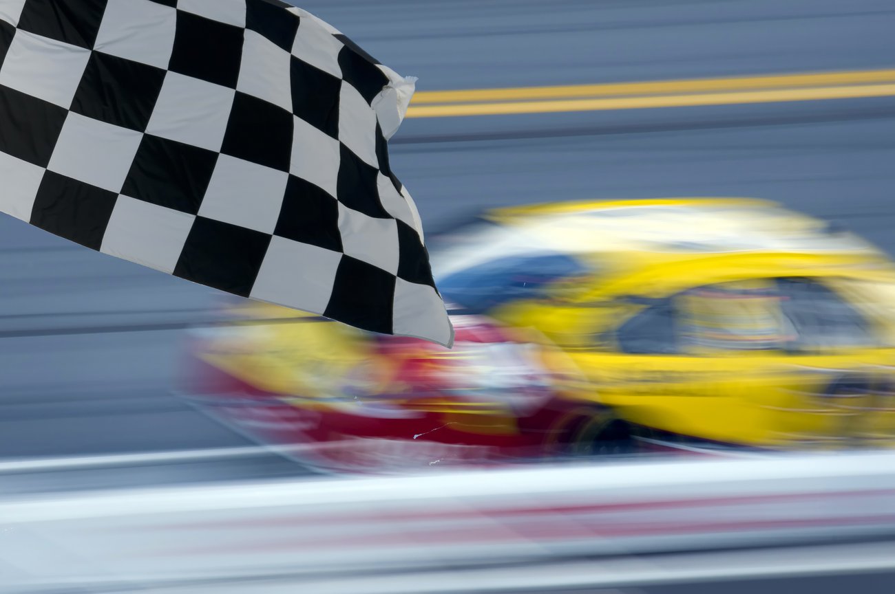 Checkered flag over a blurred race car at the finish line, symbolizing velocity